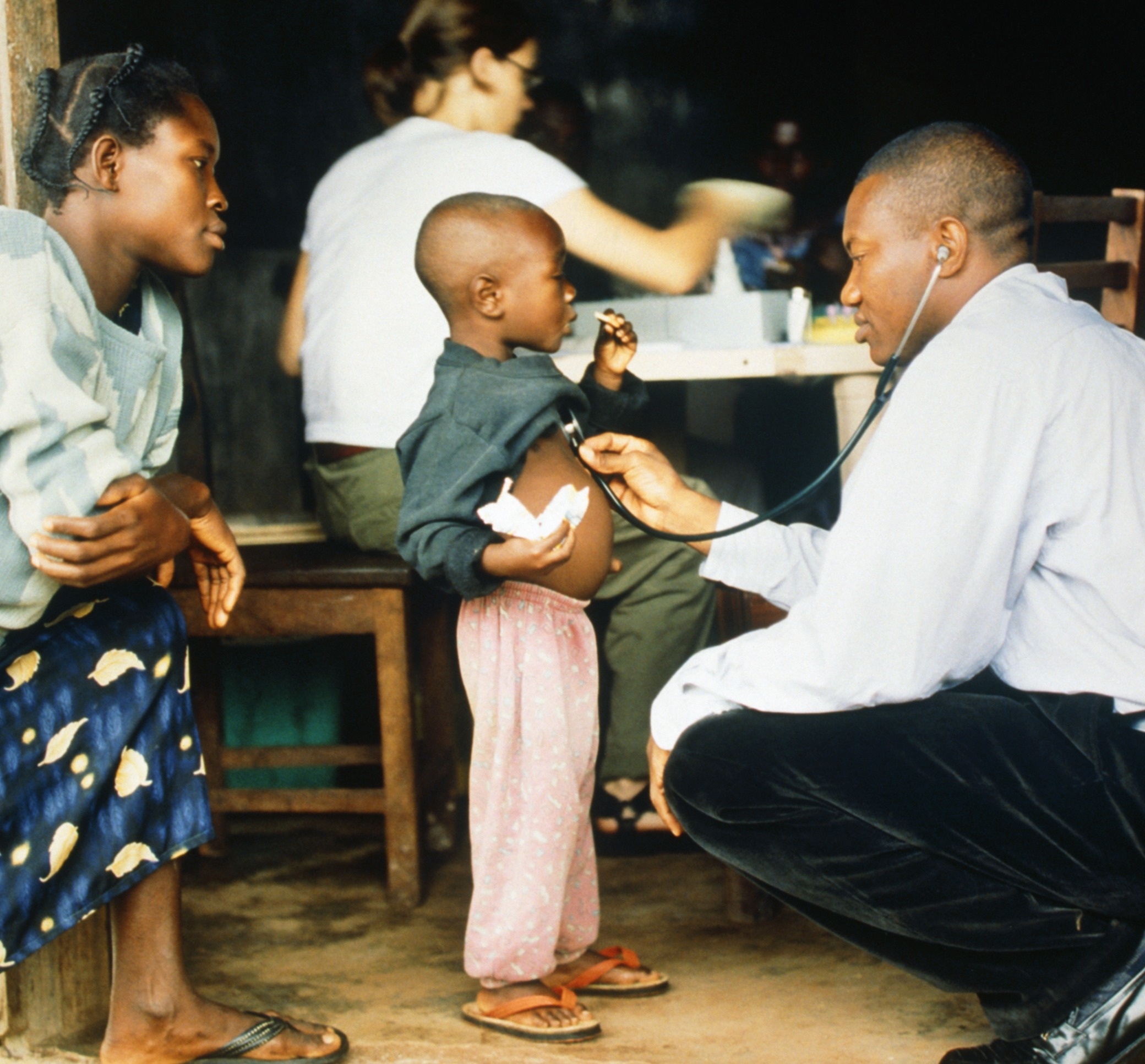 Healthcare worker with stethoscope examines a child while a woman watches