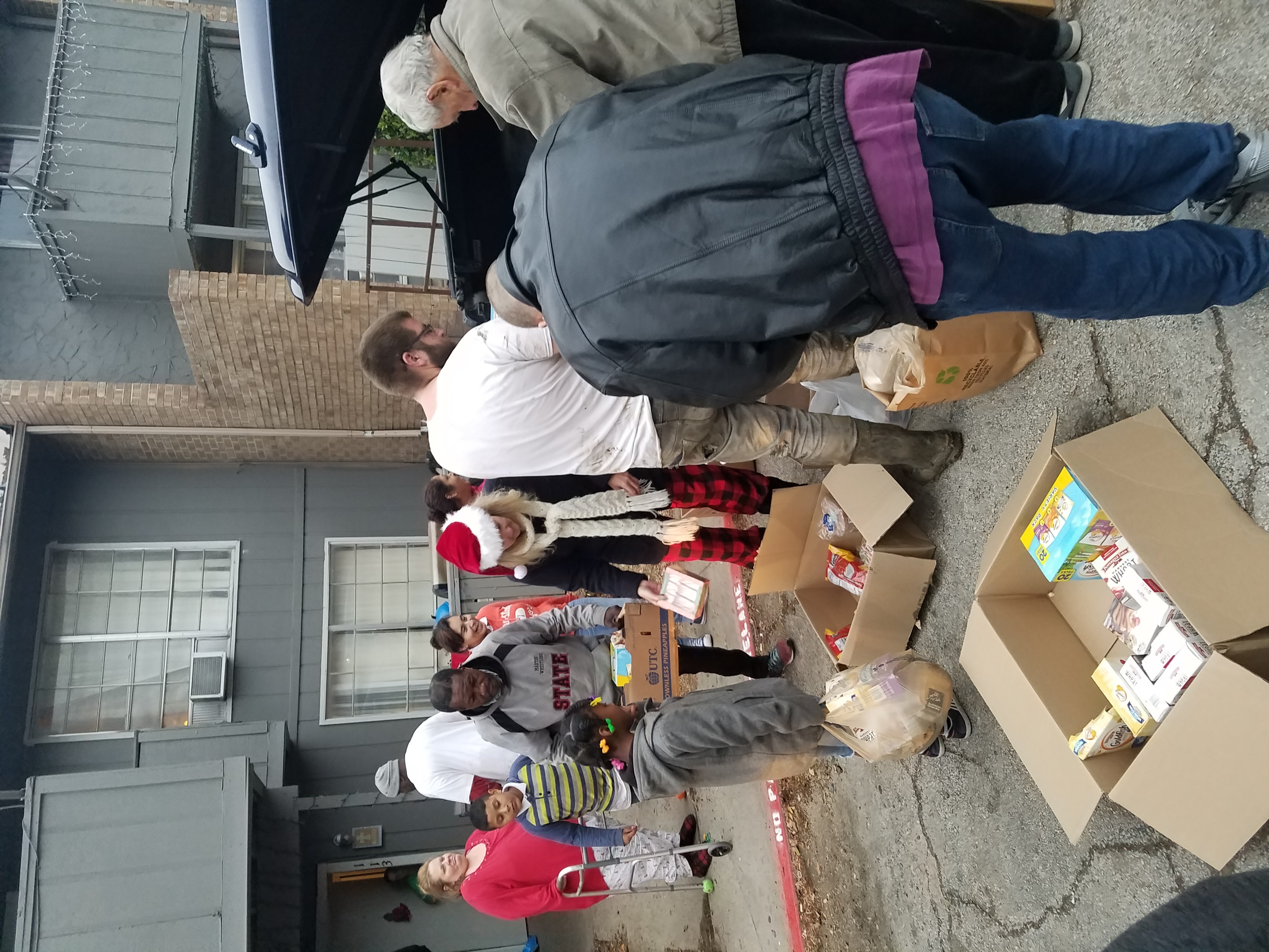 People stand beside tables and boxed goods outside a building