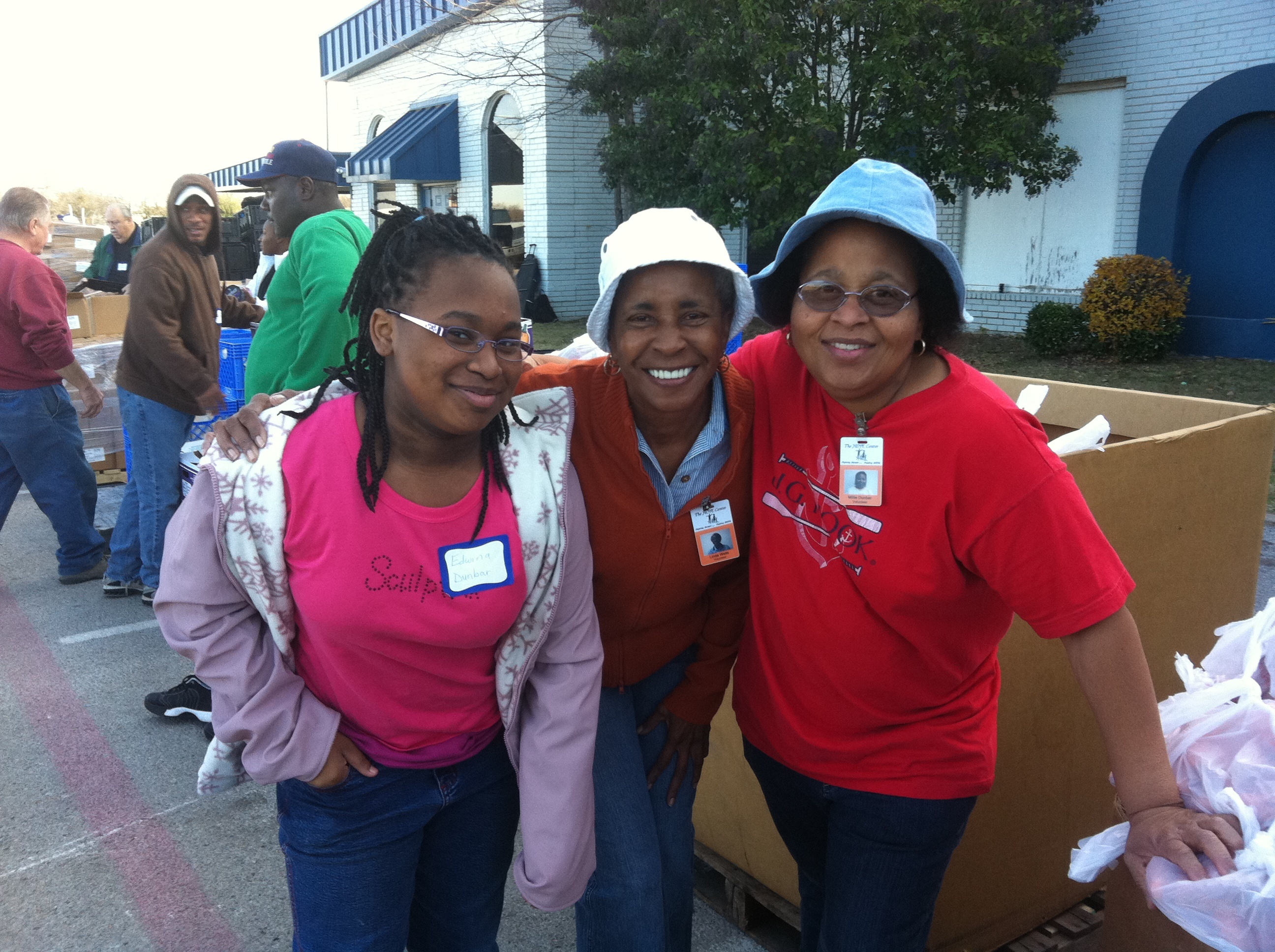 Three women with Hope Center badges beside boxed goods outdoors