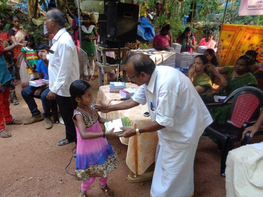 An adult in white bends toward a child amid a group outdoors