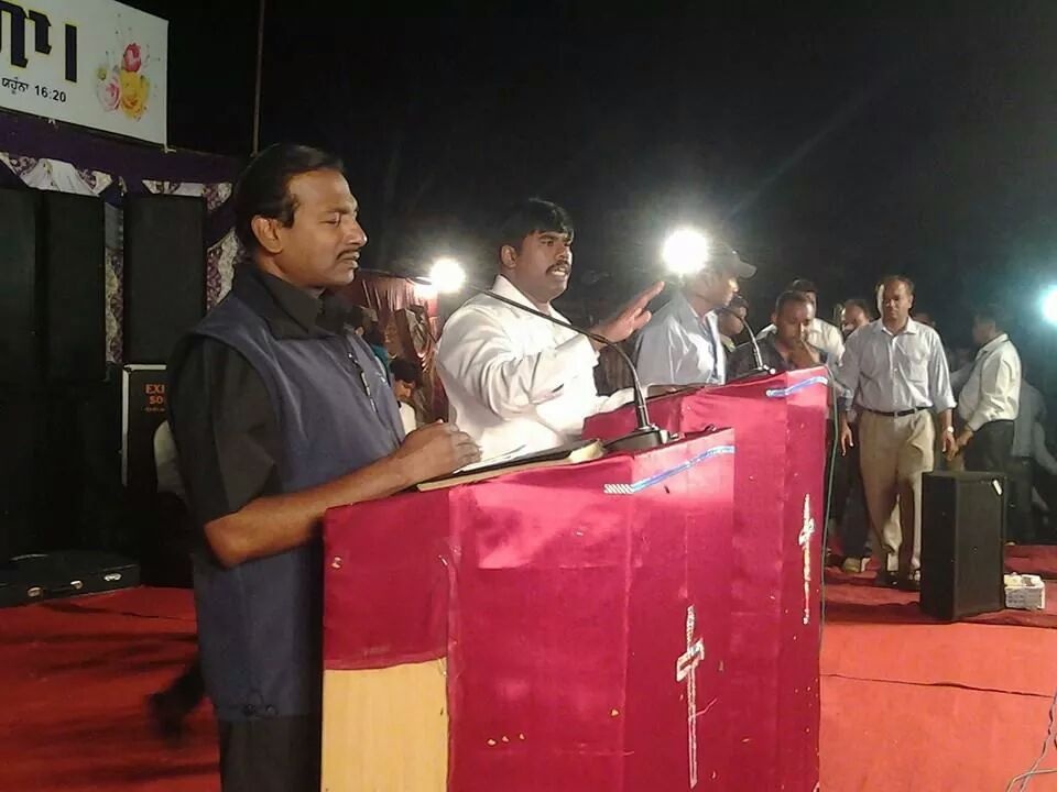 A man stands at a red podium with other people on a lit stage