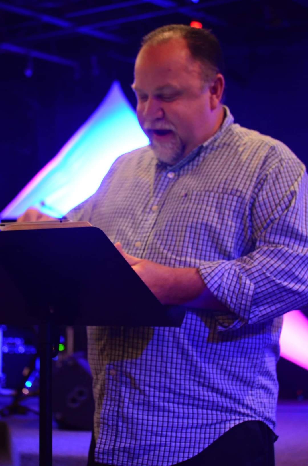 A man stands at a podium under colored lighting